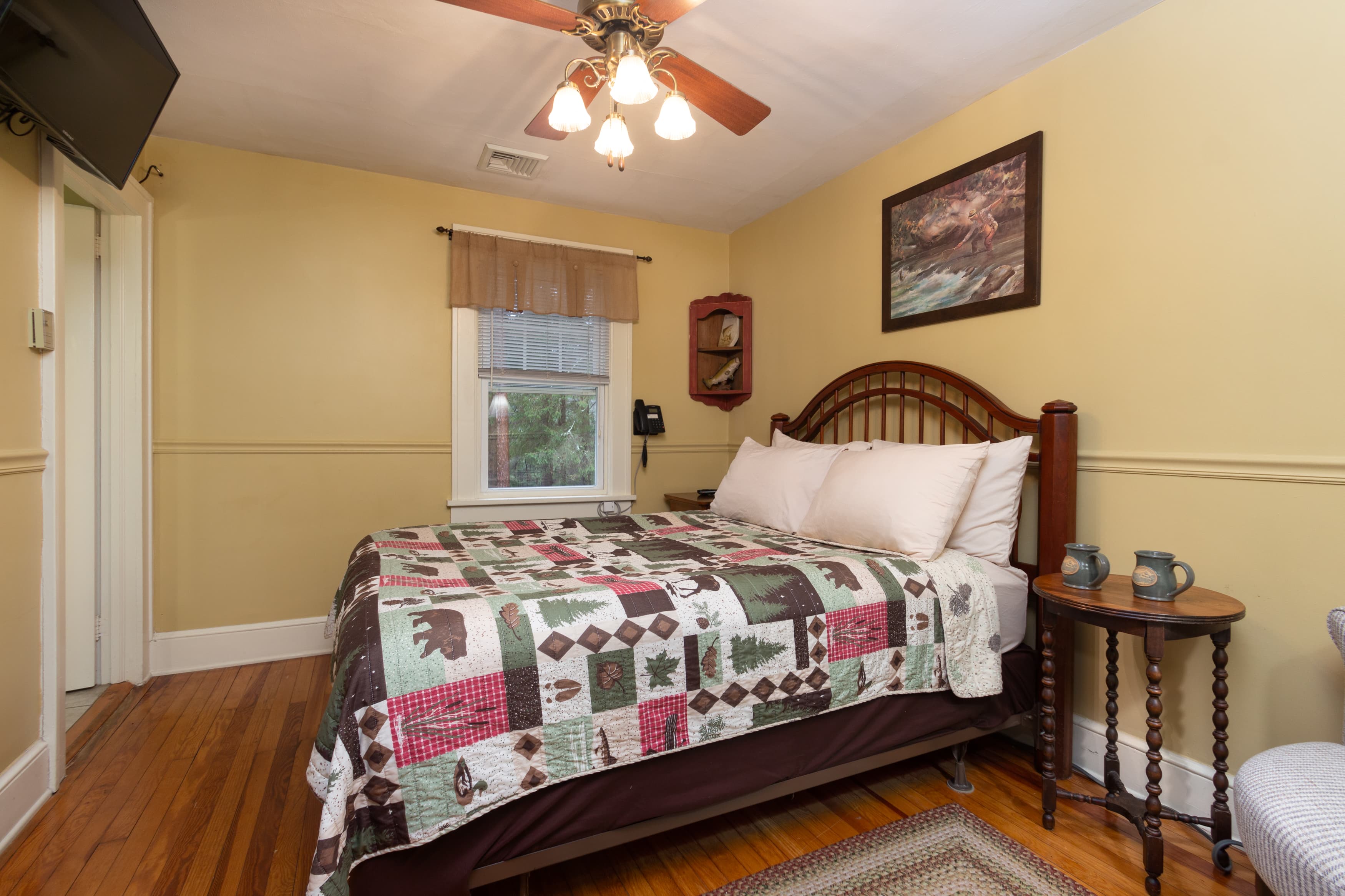 A cozy bedroom with a dark wood bed, a bear-patterned quilt, bright yellow walls, hardwood floors, and a ceiling fan.