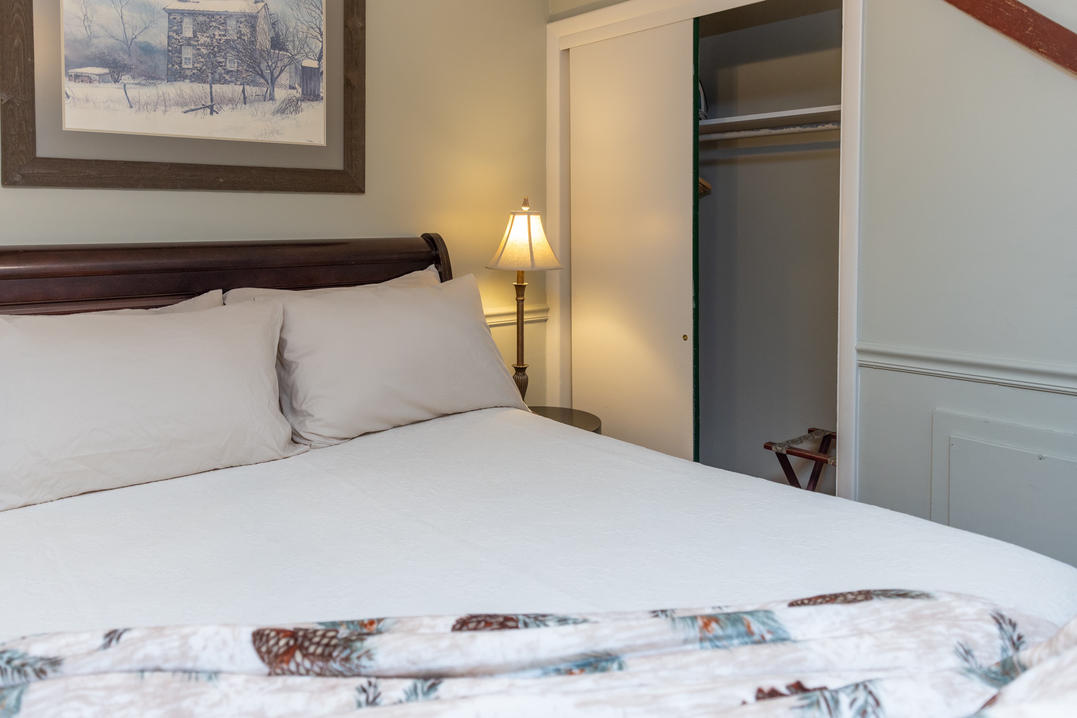 A close-up of a dark wood sleigh bed with a white duvet and a patterned throw, next to an open closet with sliding doors.