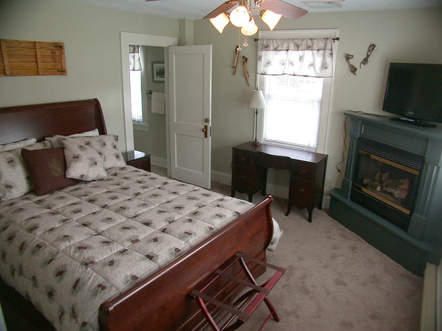 A bedroom with a dark wood sleigh bed, a gas fireplace with a blue surround, and a desk by the window against light green walls.