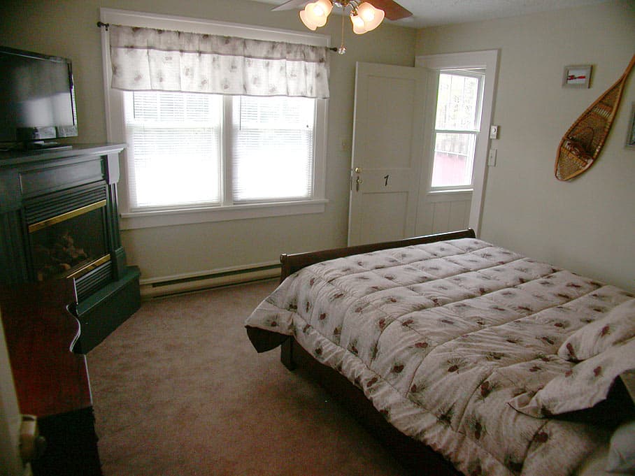 A bedroom with a queen bed and a floral comforter, featuring a black fireplace, a wall-mounted TV, and snowshoe decor.
