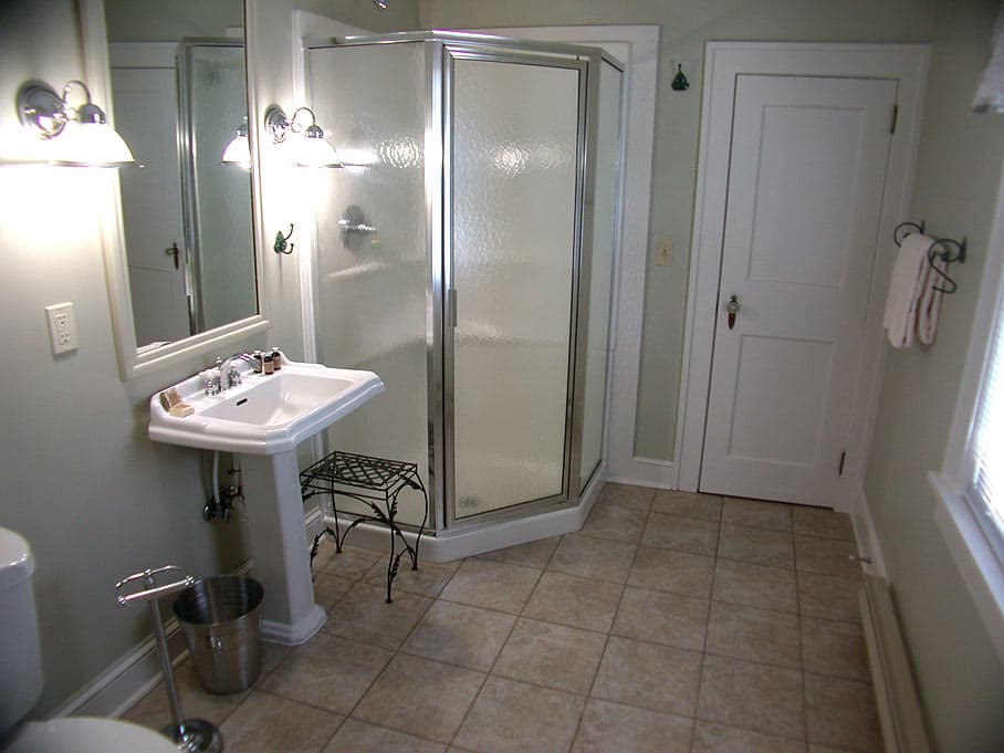 A spacious bathroom with light green walls, a corner glass shower enclosure, and a white pedestal sink and toilet.