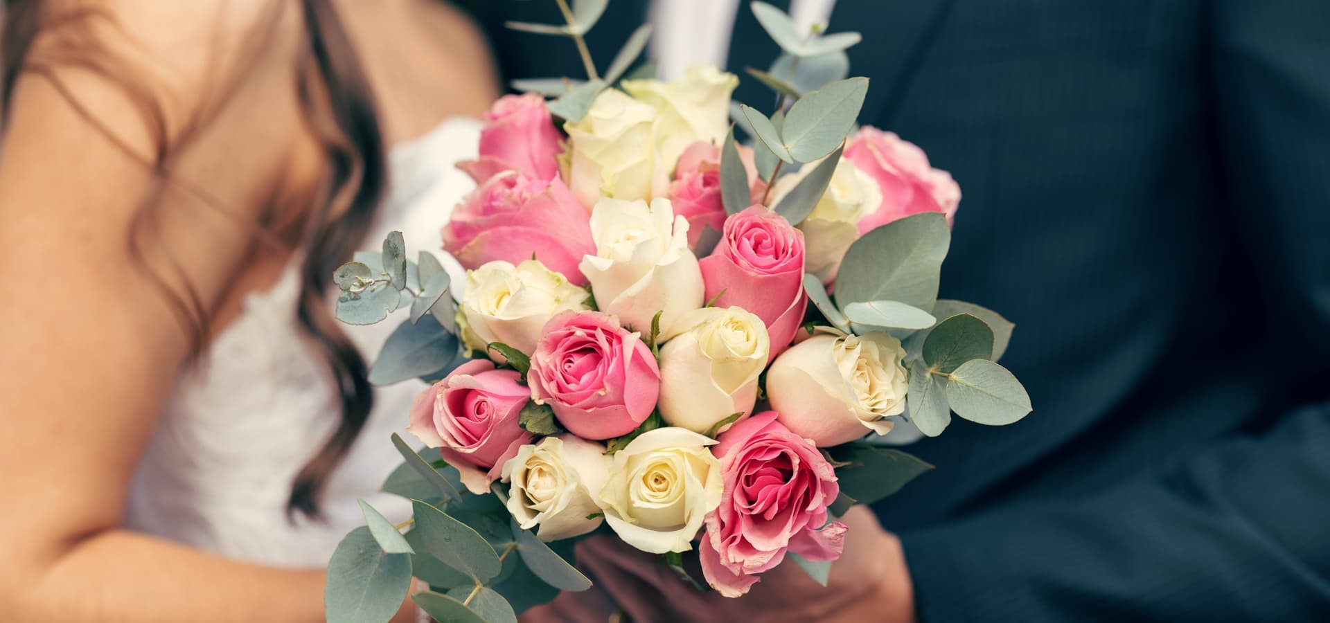 A bride holds a bouquet of pink and white roses with eucalyptus leaves.