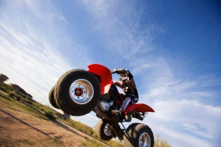 A rider jumps an ATV against a bright blue sky.