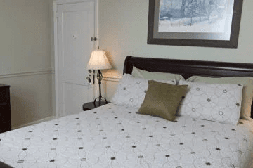 A cozy bedroom featuring a wooden bed with patterned bedding, a nightstand lamp, and framed artwork on the wall.