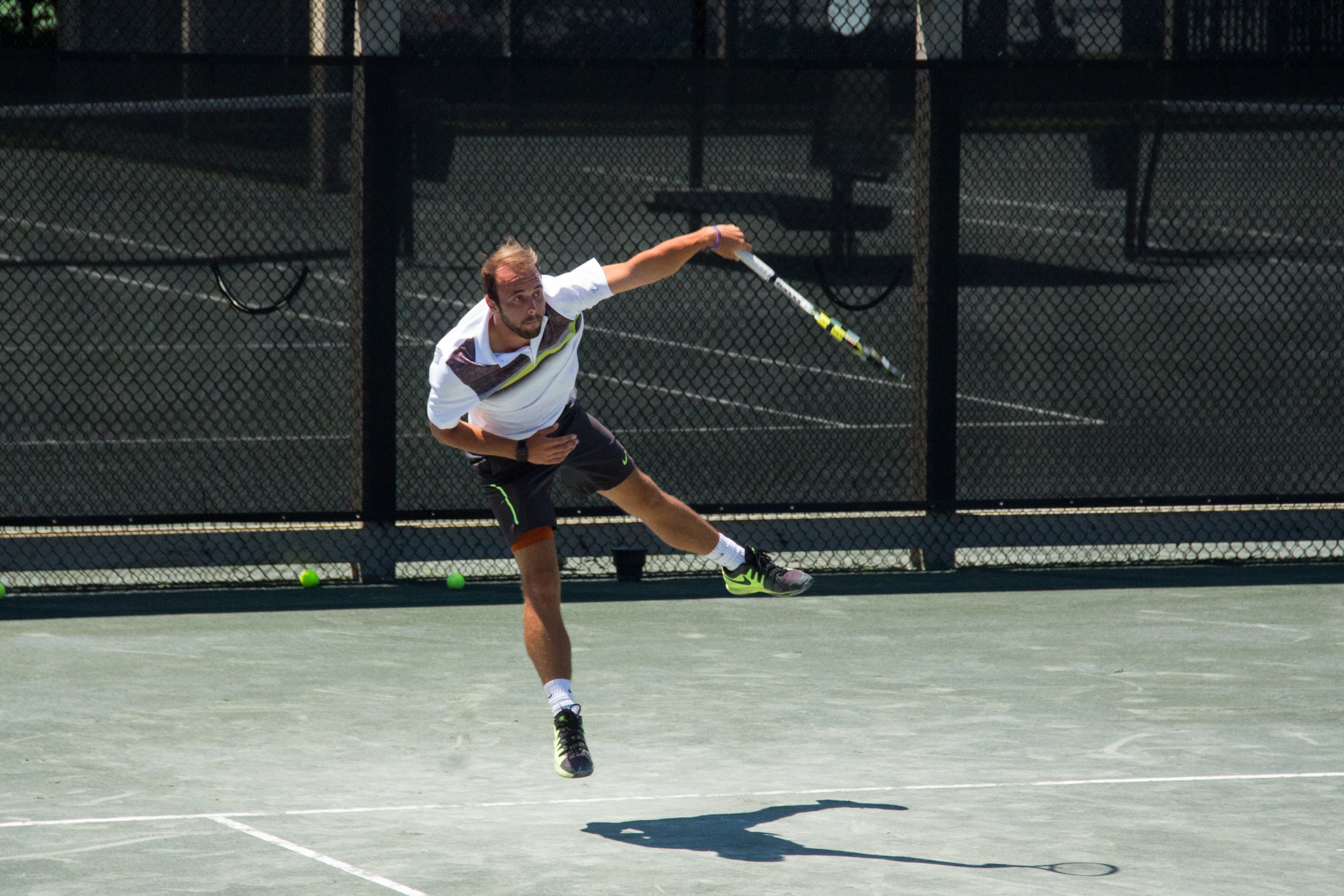 A male tennis player jumps while executing a forehand shot.