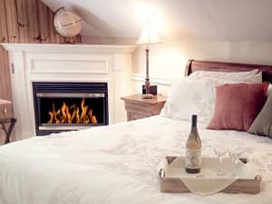Cozy bedroom with a wine bottle and glasses on a tray, next to a fireplace.