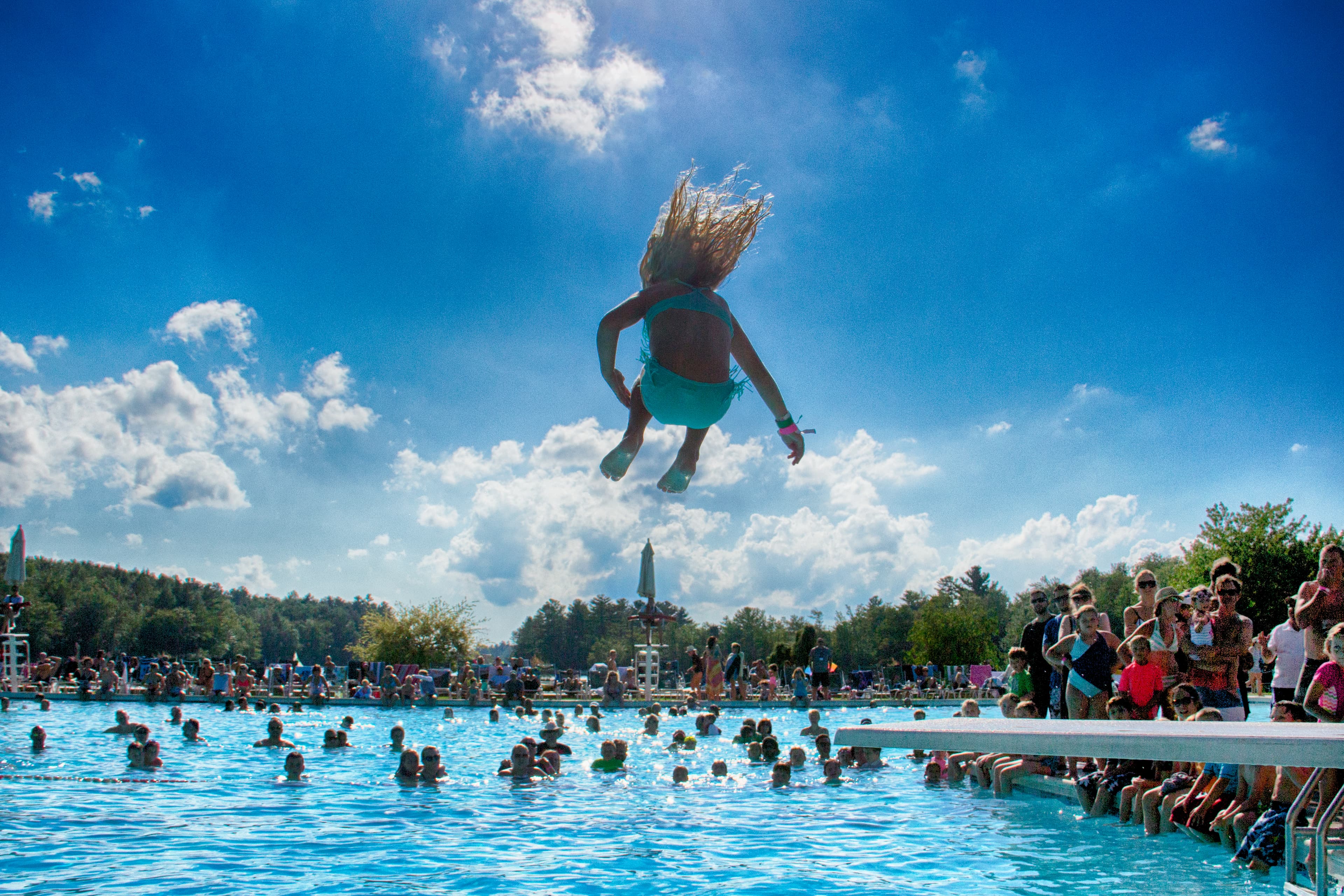 A child leaps into a crowded swimming pool on a sunny day.