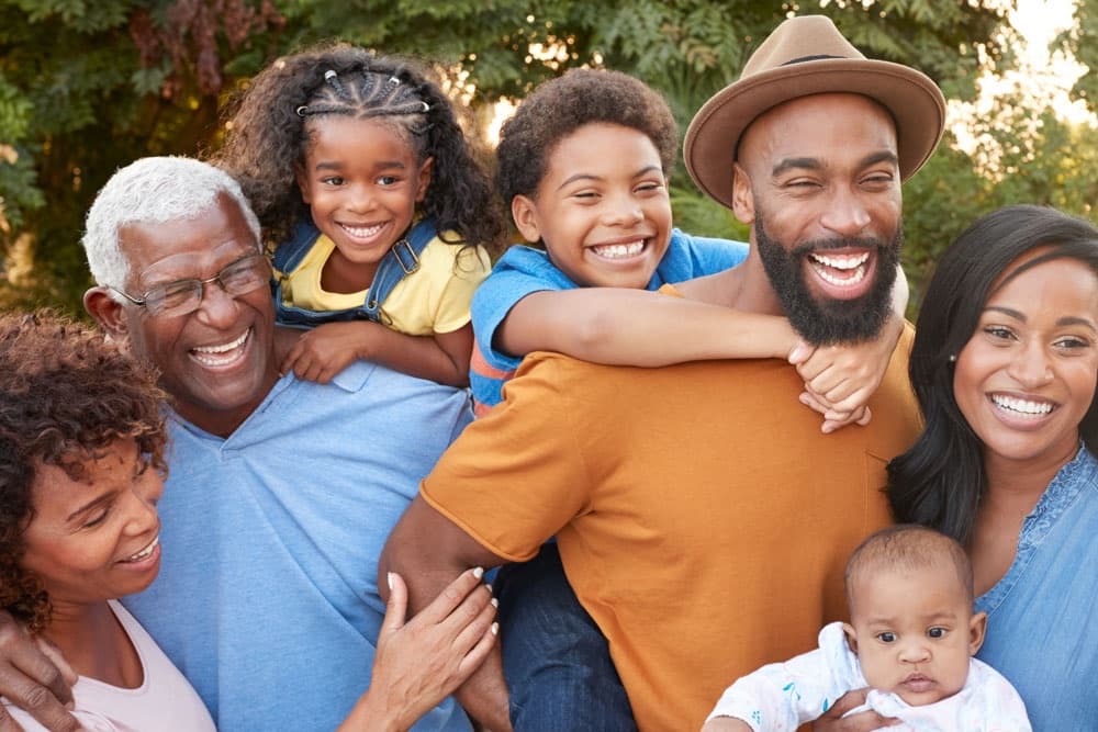 A joyful multi-generational family poses outdoors, smiling and laughing together.