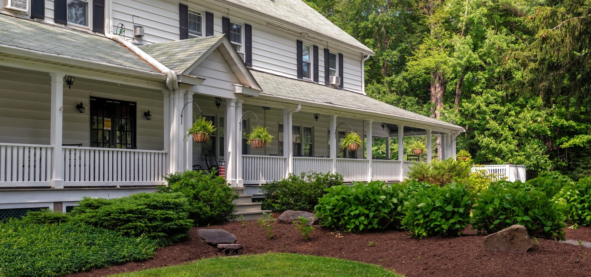 A charming white house with a porch, surrounded by lush greenery and manicured gardens.
