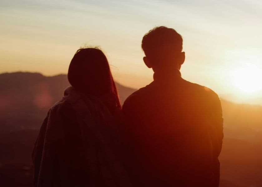 A couple watches the sunset from a mountain view.