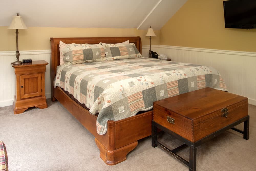 A cozy bedroom featuring a wooden bed with a patterned quilt, accompanied by a bedside table and a storage trunk.