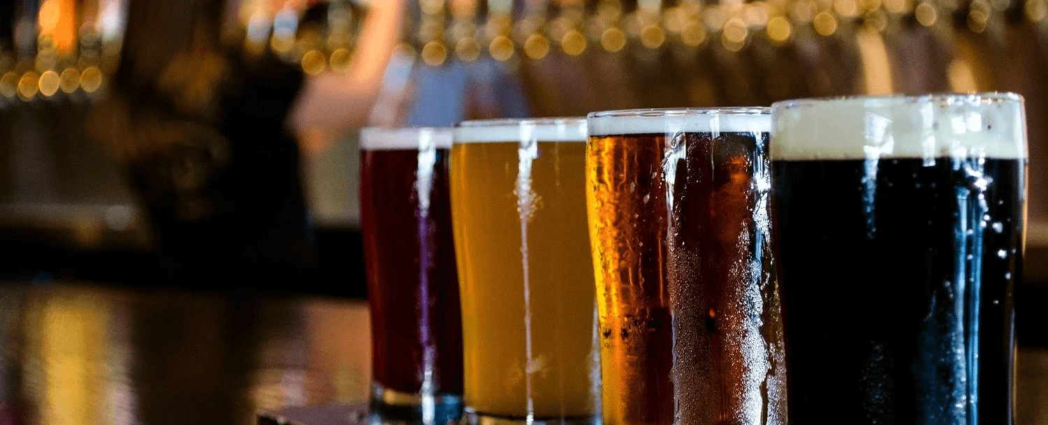 A row of five different craft beers in glasses on a bar countertop.