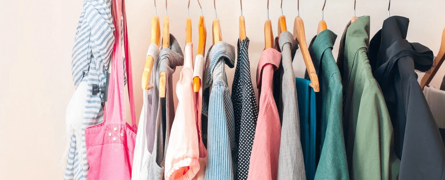 A colorful assortment of clothing hanging on wooden hangers against a pale wall.