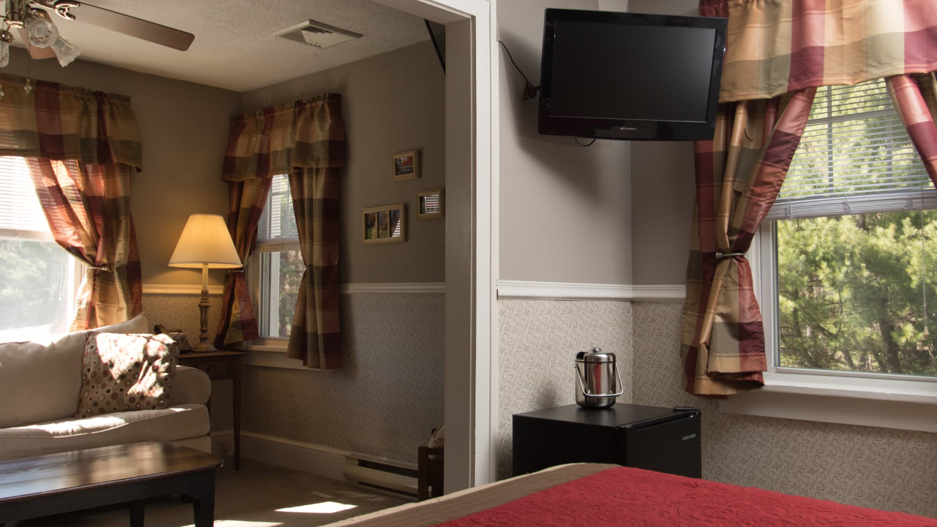 A cozy hotel room featuring a living area with a sofa, lamp, and wall-mounted TV.