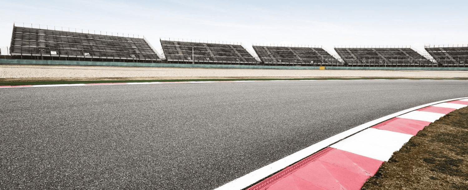 A racetrack curves with empty grandstands in the background under a clear sky.