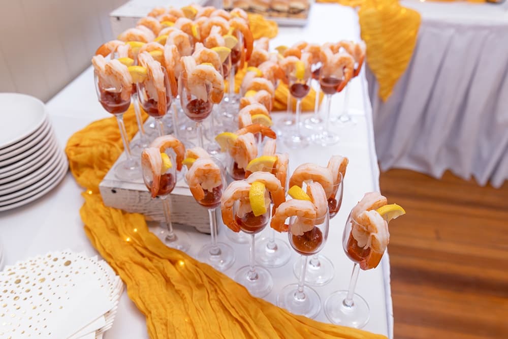 A table filled with shrimp cocktails garnished with lemon in elegant glasses.