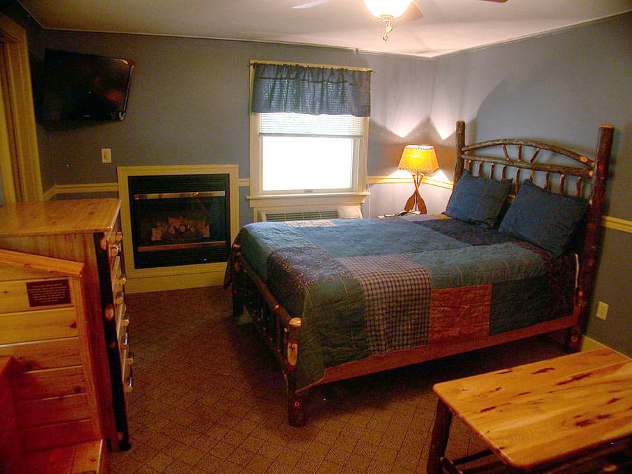 A cozy bedroom with a rustic spindle bed, a built-in gas fireplace, a TV, and log-style furniture against a blue wall.