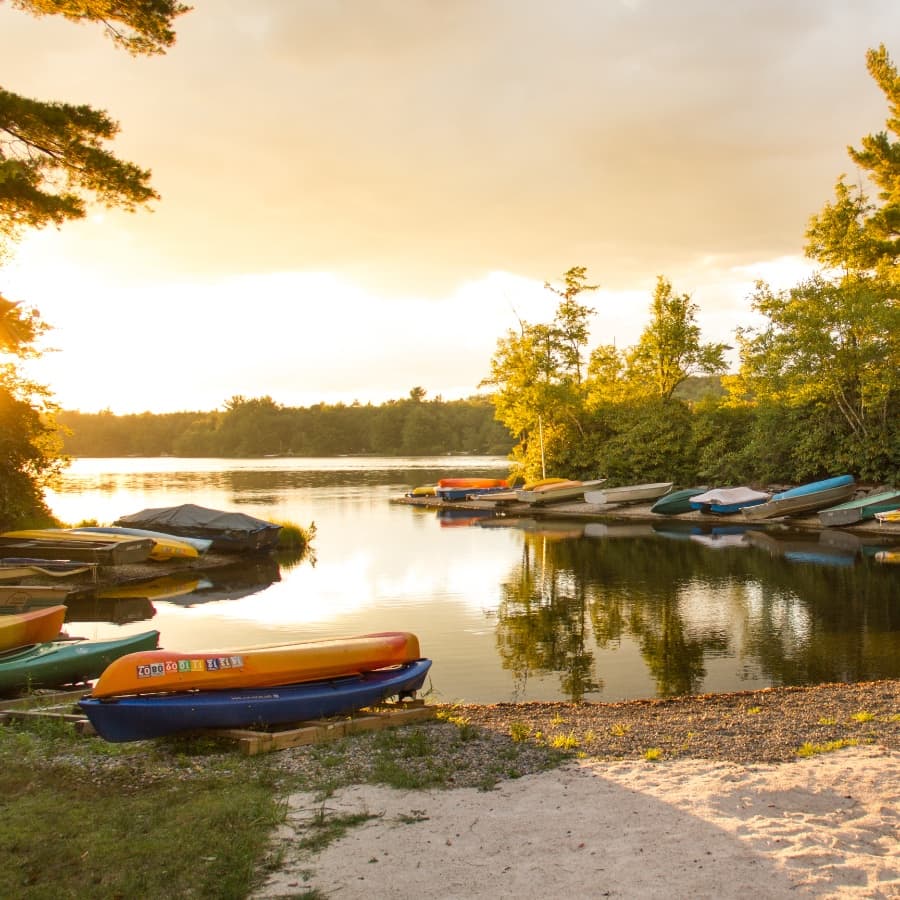Sunset over a peaceful lake with colorful kayaks lined along the shore.