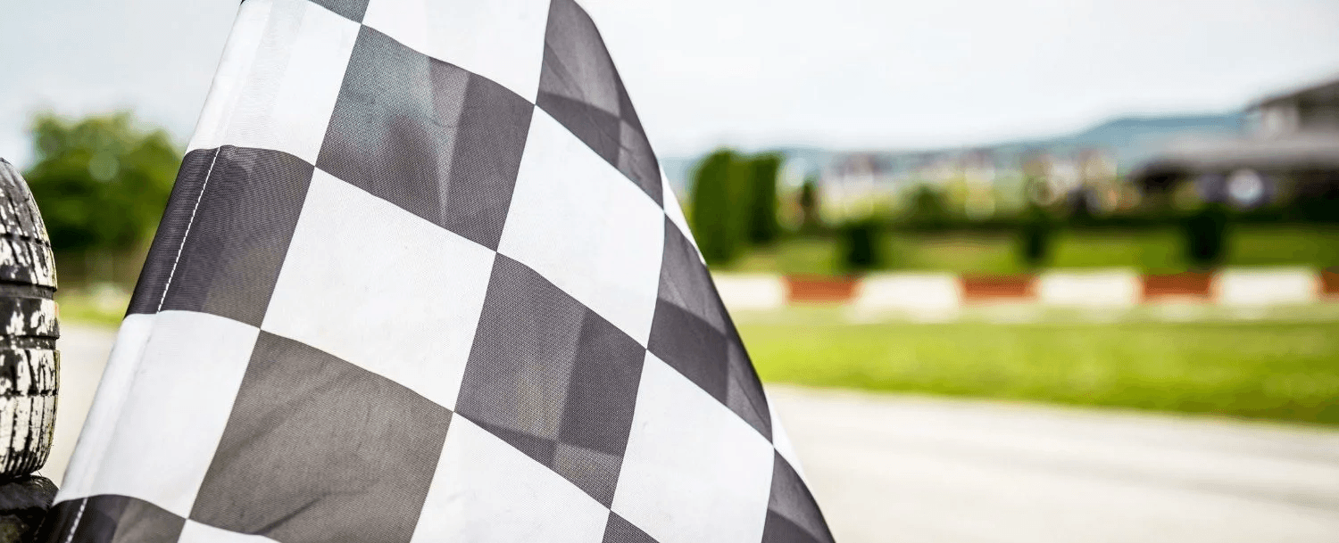 A close-up of a checkered racing flag against a blurred racetrack background.