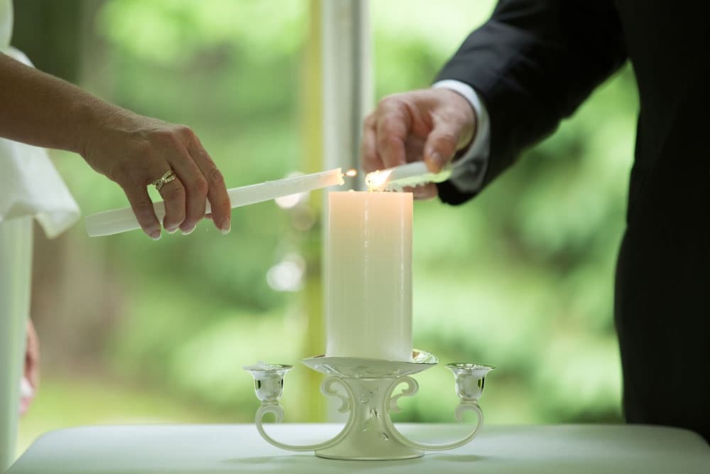 Two hands light a white candle together during a ceremony.