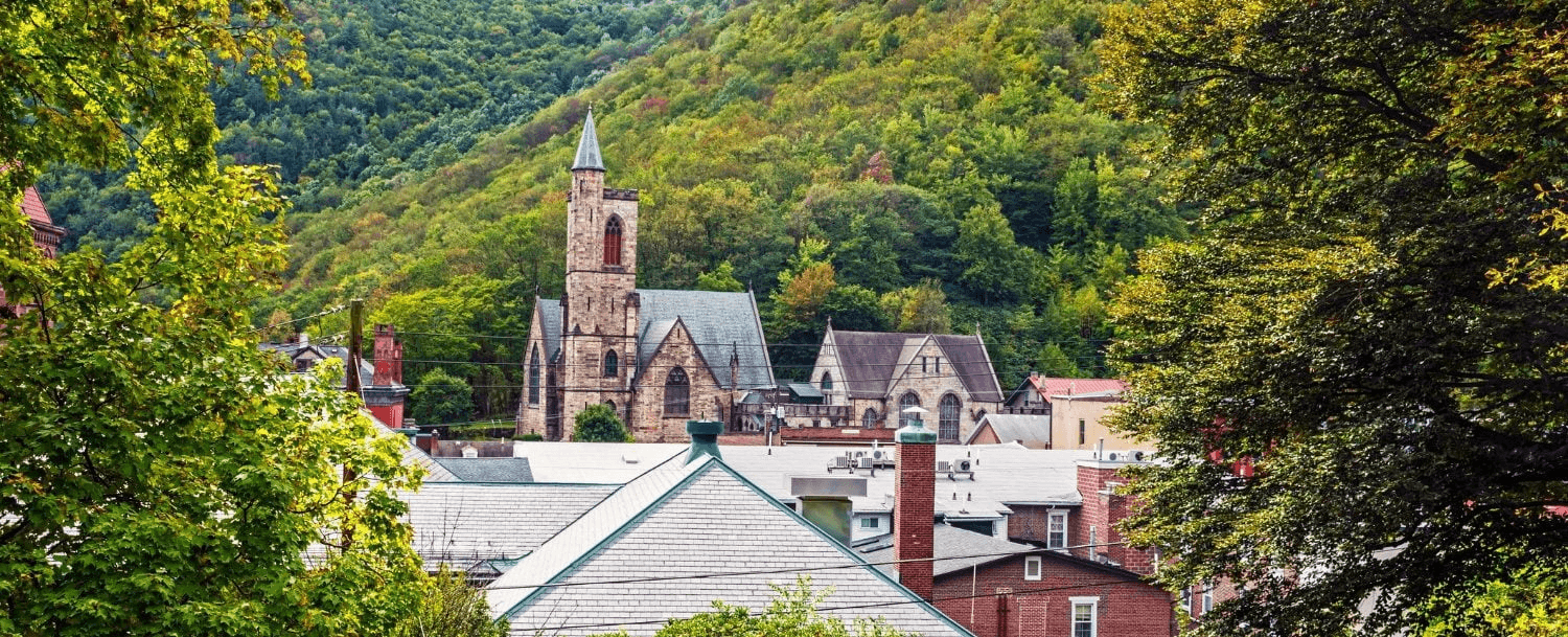Scenic view of a village with a church surrounded by trees and mountains.