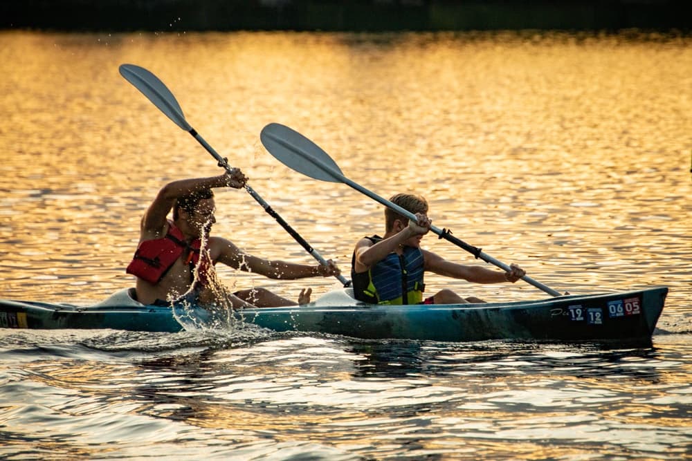 Two people kayaking on a calm lake during sunset.