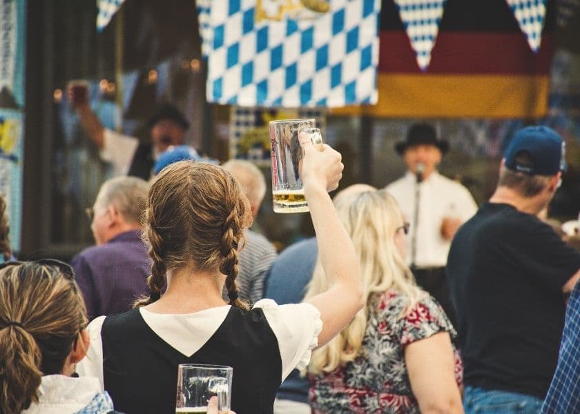 A crowd enjoys a festive event, with a woman in traditional attire raising a beer mug.