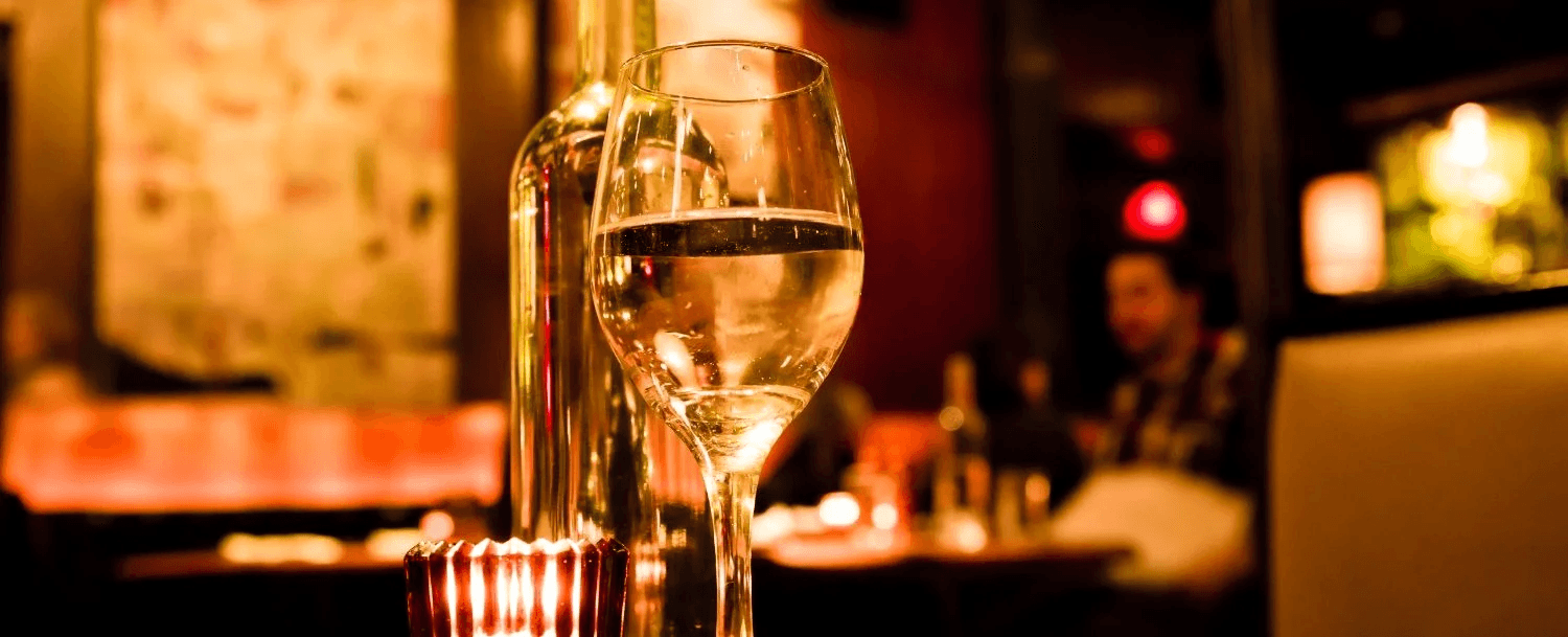 A close-up of a wine glass and bottle in a dimly lit restaurant setting.