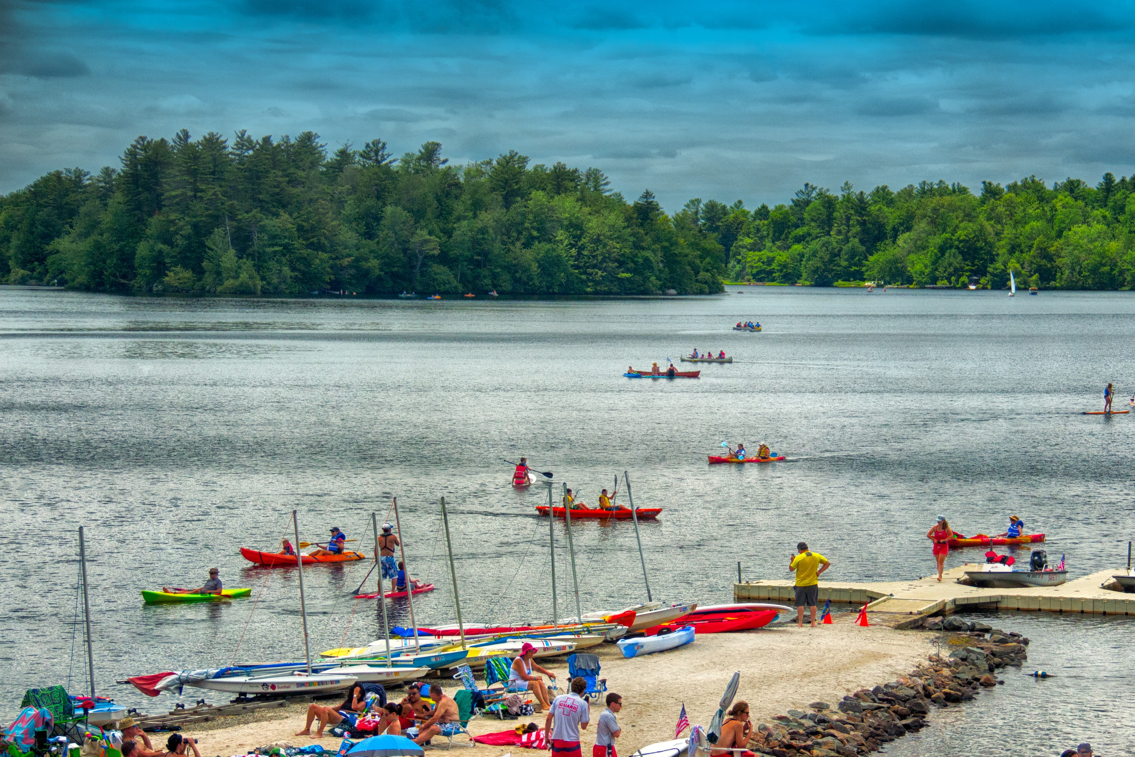 A scenic lakeside view with people kayaking and relaxing on the shore.
