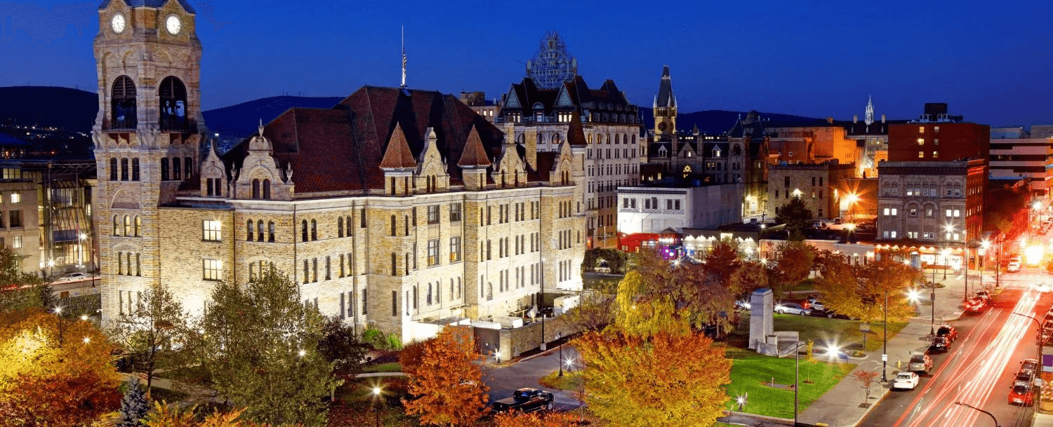 Historic buildings illuminated at night, surrounded by autumn trees and city lights.