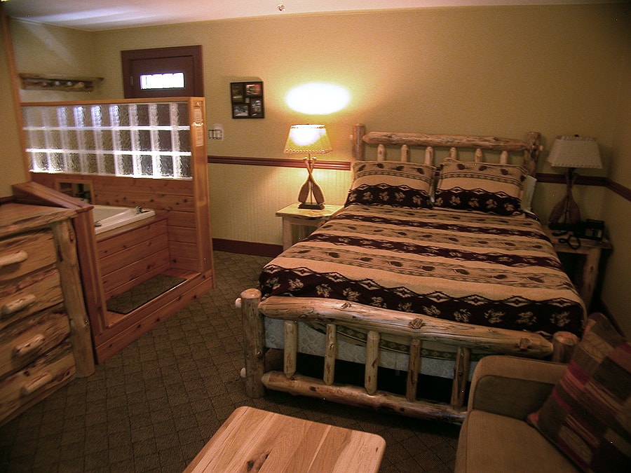 A rustic-themed room with a log-style bed, a wooden dresser, and a jetted tub enclosed by wood paneling and glass blocks.