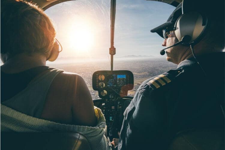 A view from inside a helicopter showing a pilot and a passenger during sunset.