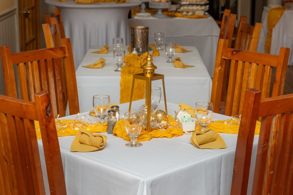 A beautifully arranged dining room with wooden chairs, tables dressed in white linens, and yellow accents.