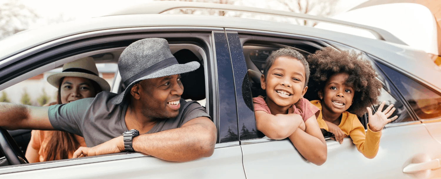 A happy family enjoys time together in a car, with parents and two children smiling and laughing.