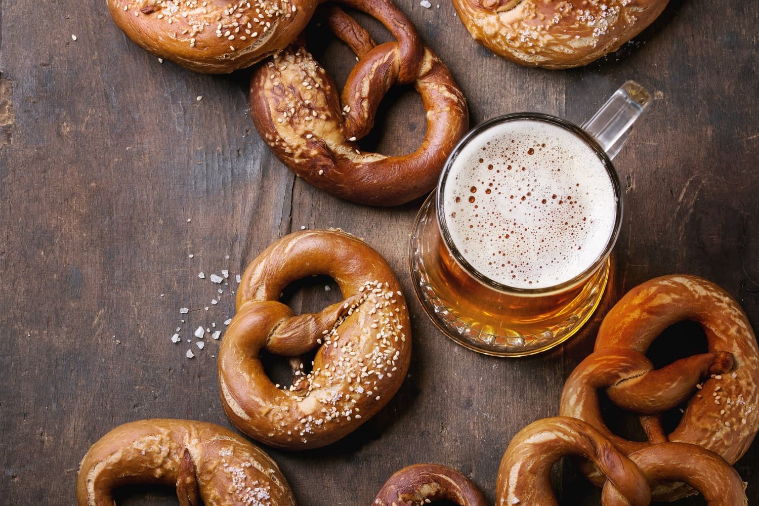 A selection of pretzels scattered around a glass of beer on a wooden surface.