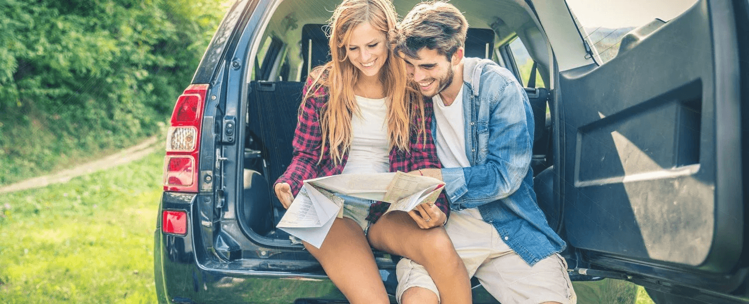 A couple sits in the back of a car, looking at a map and smiling.