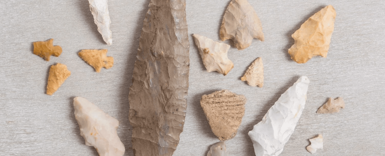 A collection of various stone tools and arrowheads arranged on a light surface.