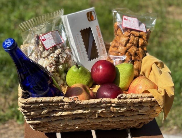 A woven basket filled with assorted fruits, snacks, and a blue bottle.