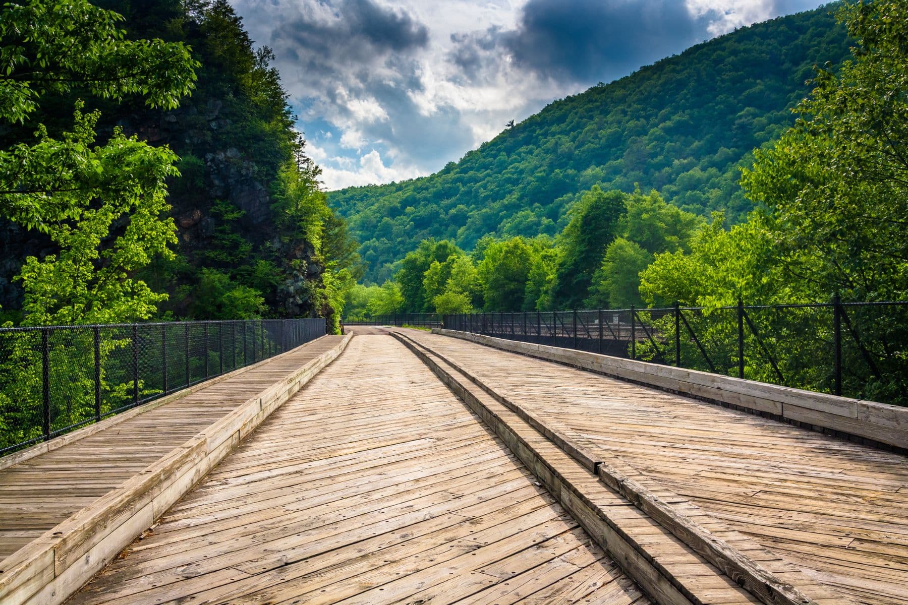 A wooden pathway stretches through lush green hills under a partly cloudy sky.