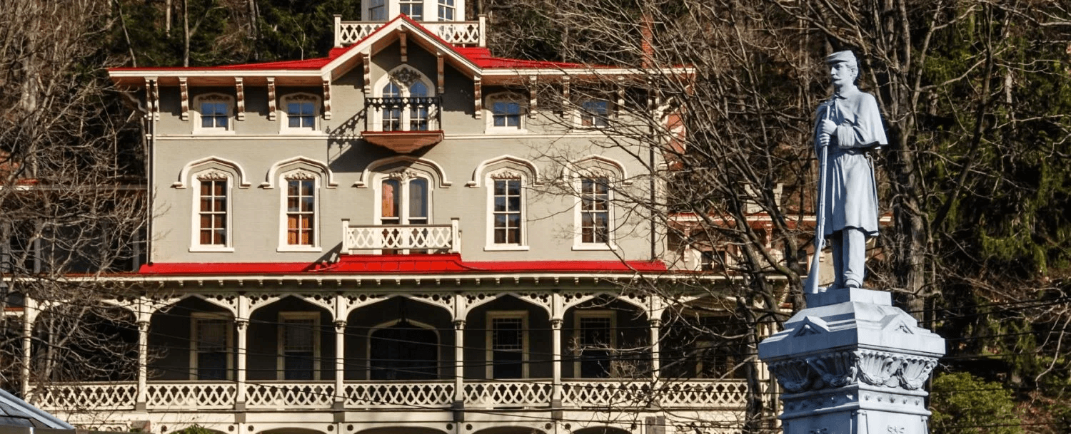 A historic mansion with a decorative upper balcony stands behind a white statue of a soldier.