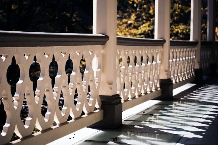 A white wooden railing with decorative cutouts casts shadows on a floor.