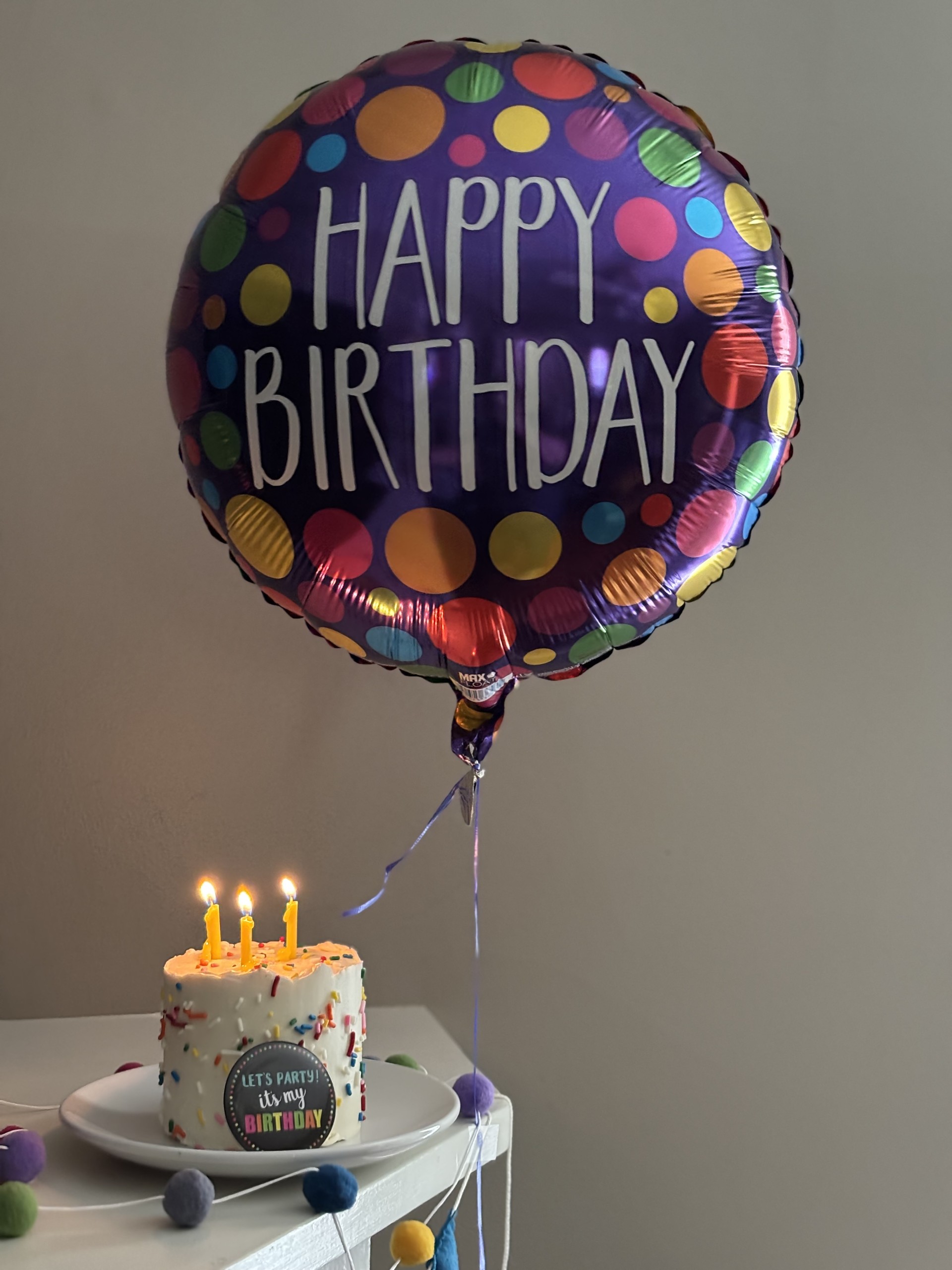 A "Happy Birthday" balloon floats above a decorated cake with candles and a festive message.