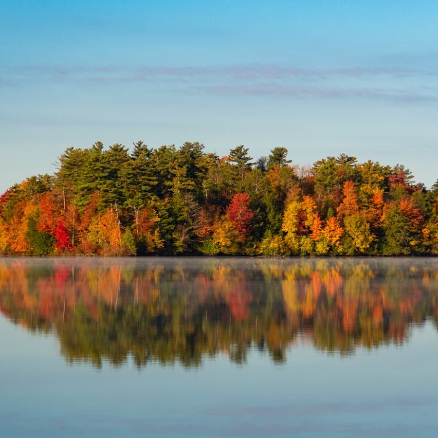 A tranquil lake reflecting vibrant autumn foliage and clear blue skies.
