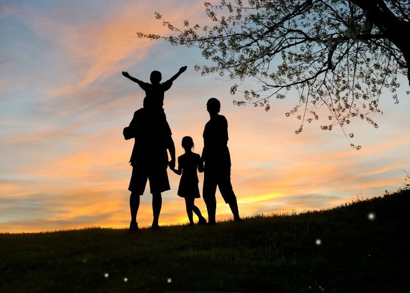 A silhouetted family enjoys a sunset, with one child on an adult's shoulders.
