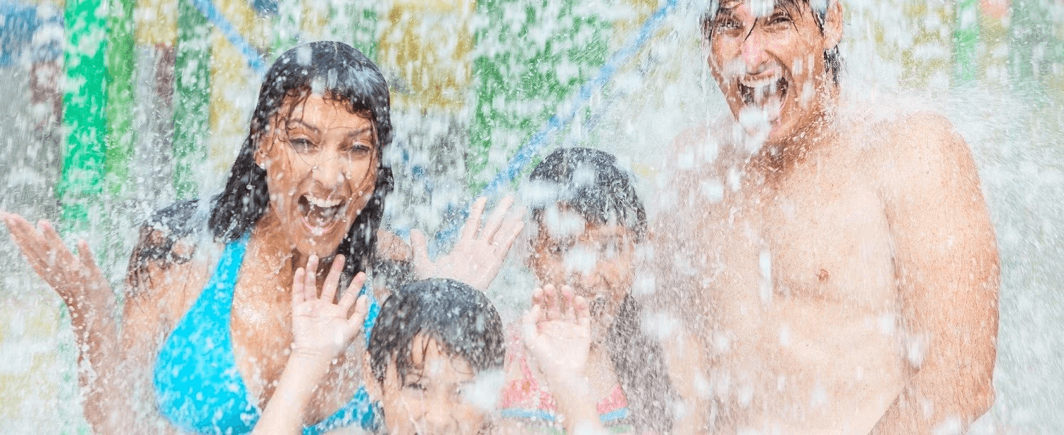 A joyful family splashes in water, smiling and having fun at a water park.