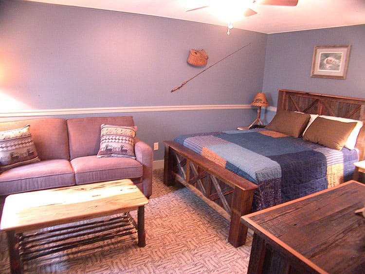A cozy bedroom with a rustic wooden bed frame, a small sofa, and a fishing rod mounted on the periwinkle blue wall.