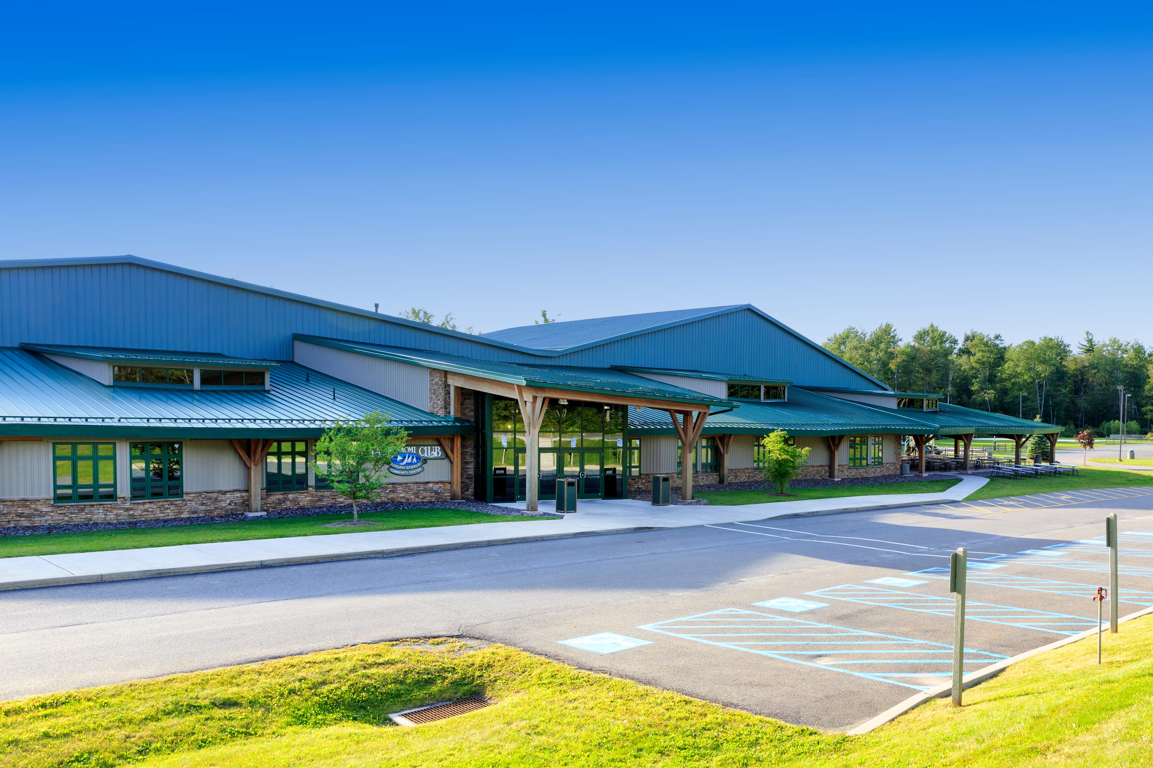 A modern building with a green metal roof and large windows, set against a clear blue sky.