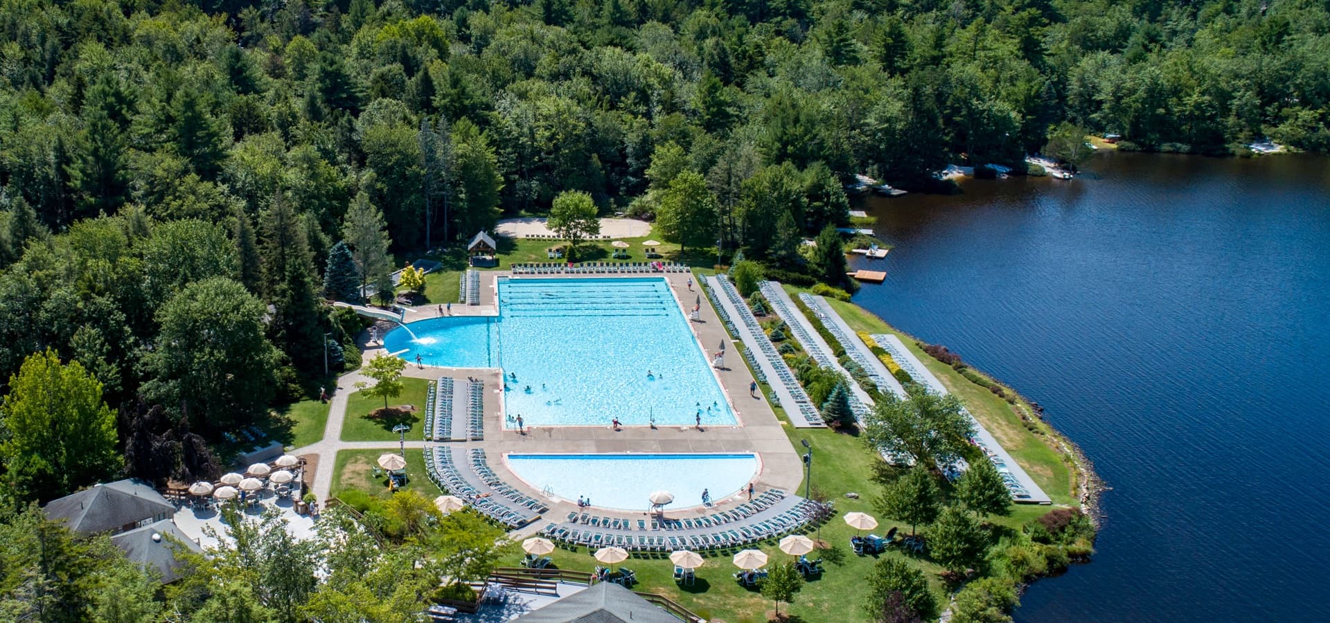 Aerial view of a large swimming pool surrounded by greenery and a lake.