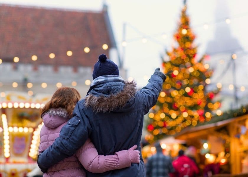 A couple embraces while admiring a Christmas tree in a festive market.