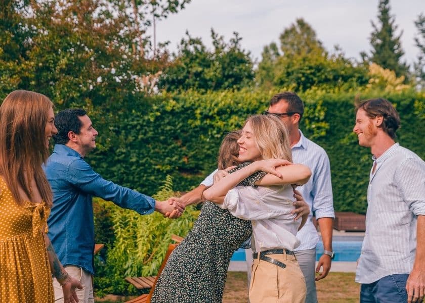 a group of friends meeting in a backyard near a pool warmly hugging and shaking hands surrounded by trees and outdoor furniture a group of friends meeting in a backyard near a pool warmly hugging and shaking hands surrounded by trees and outdoor furniture
